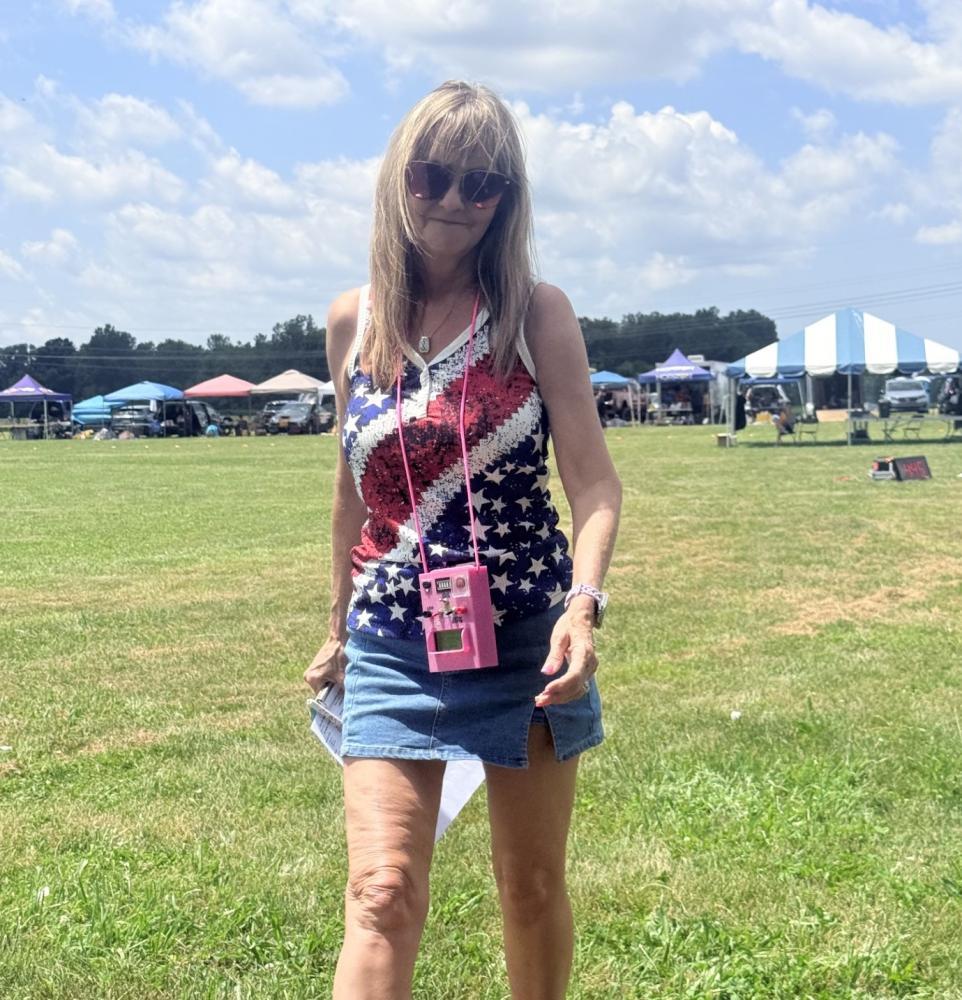 Woman outdoors on grass, wearing a patriotic tank top and denim skirt, sunny day.