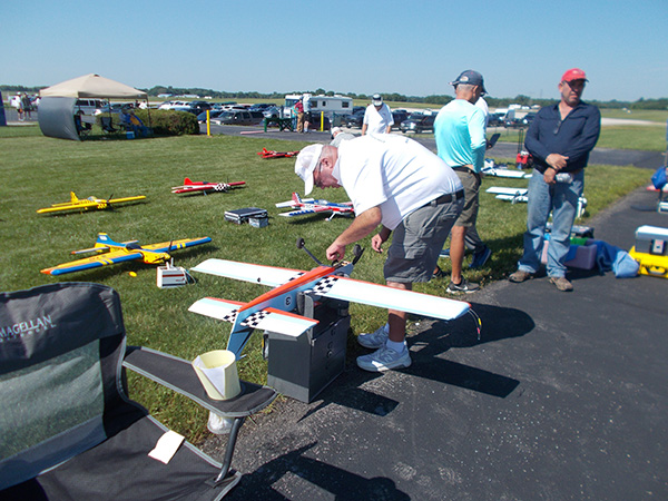 Man adjusting a model airplane outdoors with others nearby on a sunny day.
