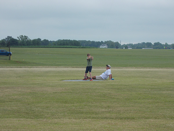Two people flying CL on a grassy field under a cloudy sky.