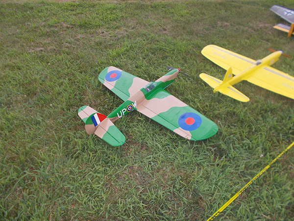 Toy planes on grass, one camouflaged, another yellow.