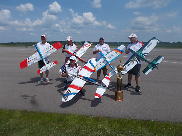 Four people with model planes and a trophy on a tarmac.