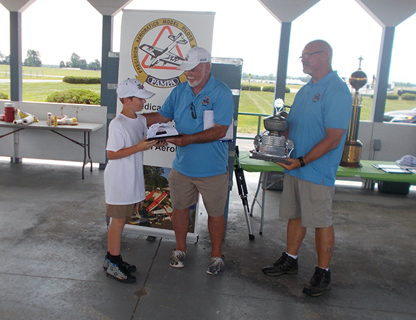 Award ceremony with three people; child receiving a book from two adults.