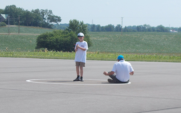 Two people on an outdoor basketball court; one standing, one sitting.