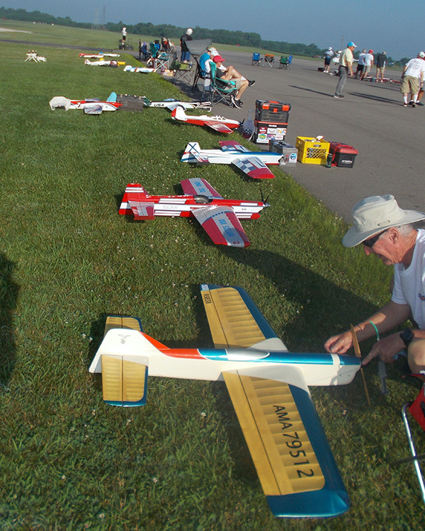 Model airplanes lined up on grass at an outdoor event, people in the background.