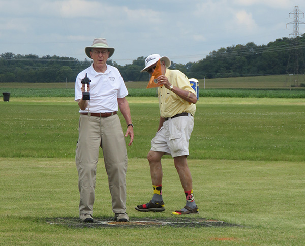 Two men in hats standing on a grassy field, one holding a bottle.