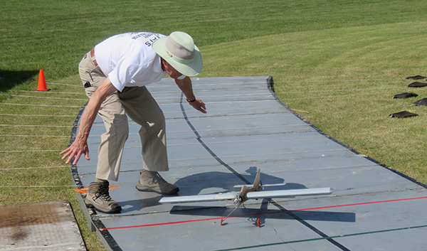 Man guiding a small model plane on a runway outdoors.