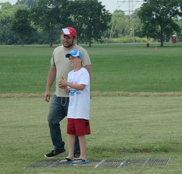 Man and boy stand in grassy field, holding remote control plane.