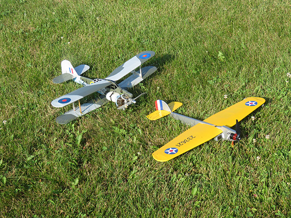 Two model airplanes on grass; one gray, one yellow, both with military insignia.