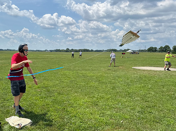 Man flies model airplane in grassy field under cloudy sky.