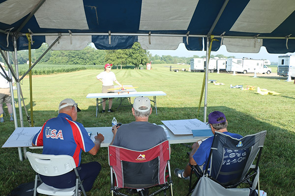 Three judges seated under a canopy at a rural outdoor event.