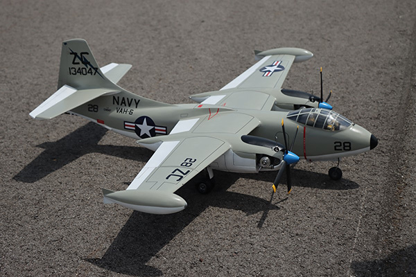 Model navy airplane with gray body and propellers on runway.