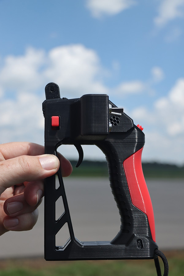 Hand holding black and red handle-like object against a cloudy blue sky.