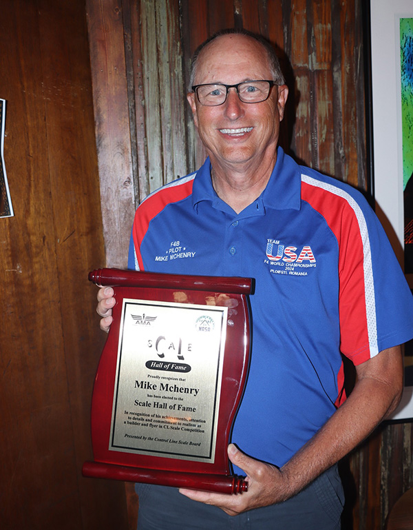 Man smiling, holding a Hall of Fame plaque, wearing a blue and red USA shirt.
