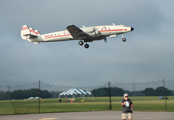 Vintage propeller plane flying low over an airfield, cloudy sky.