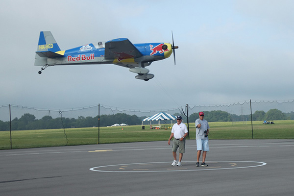 Aerobatic plane flying low above two people on an airstrip.