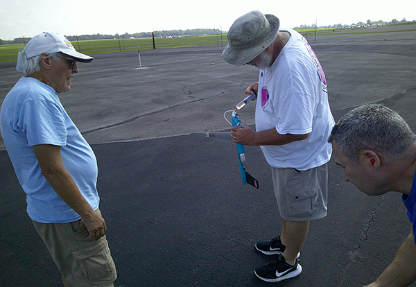 Three men on a tarmac examining a small rocket.