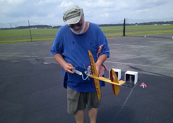 Man in blue shirt holding a yellow model airplane on a paved airstrip.