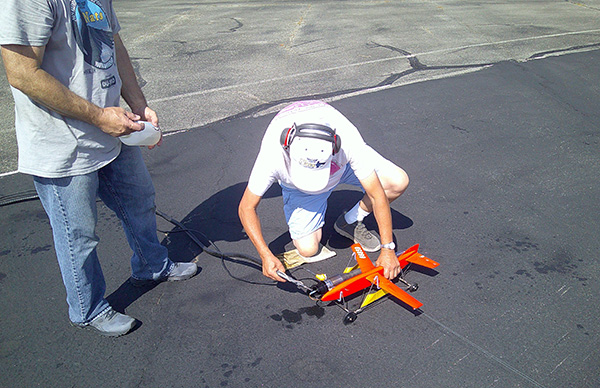 Man preparing small red drone on asphalt surface.