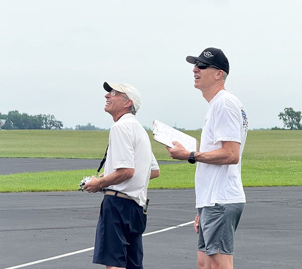 Two people watching the sky, holding a remote and a clipboard, on an overcast day.