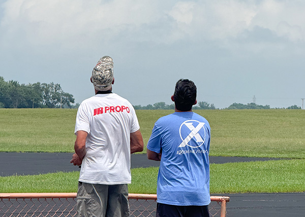 Two men watching an open field under a cloudy sky.