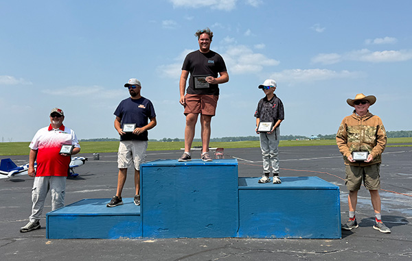Three smiling men outdoors holding bottles, sunny day.