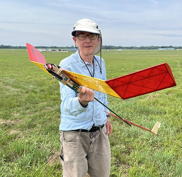 Man holding a colorful model airplane in a grassy field.