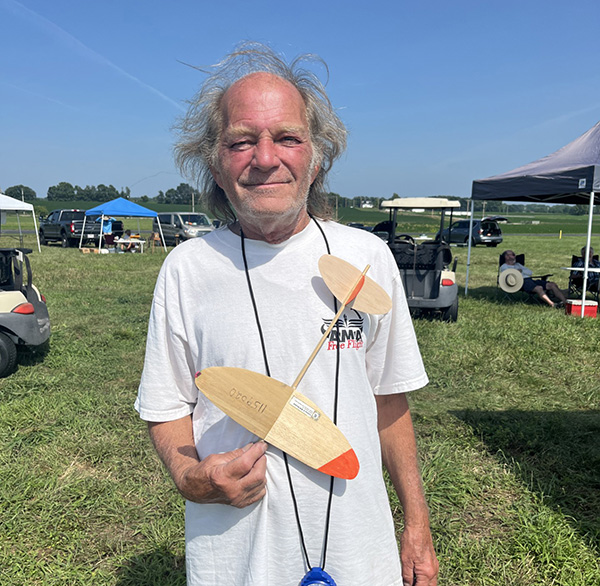 Man holding a small wooden model plane outdoors on a sunny day.