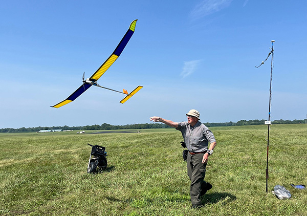 Man launching a colorful model glider in a grassy field.