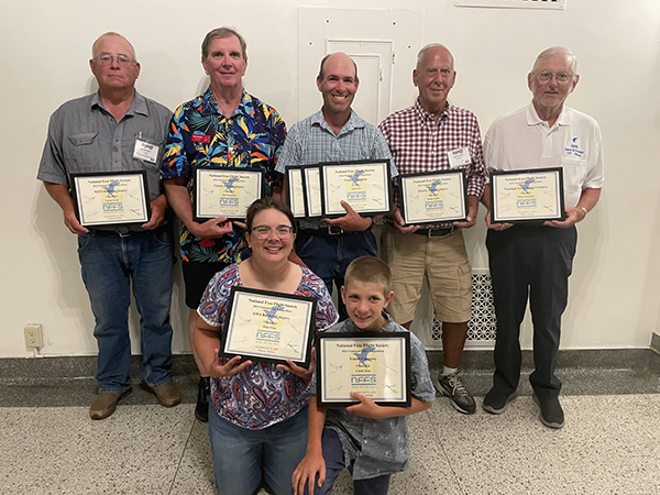 Seven people holding certificates, smiling in a bright room.
