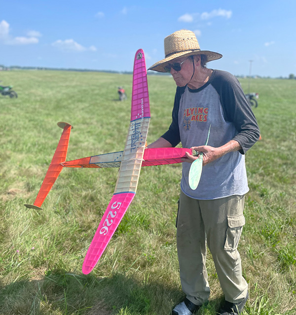 Man in a straw hat holding a pink toy glider on a grassy field.