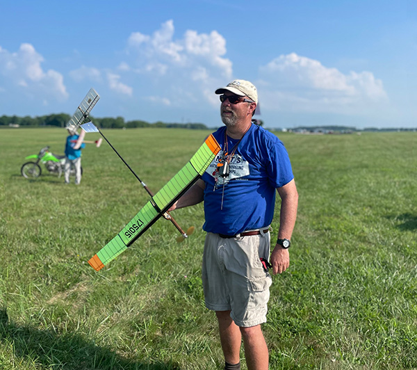 Man holding a colorful model glider in a grassy field.