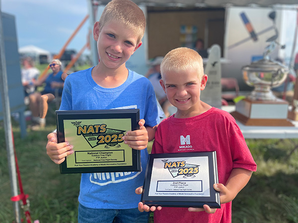 Two boys smiling, holding framed awards.