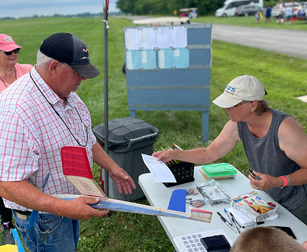 Outdoor registration table with two people exchanging documents.