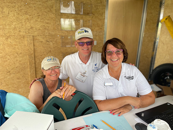 Three people smiling at a table, wearing casual attire and caps.