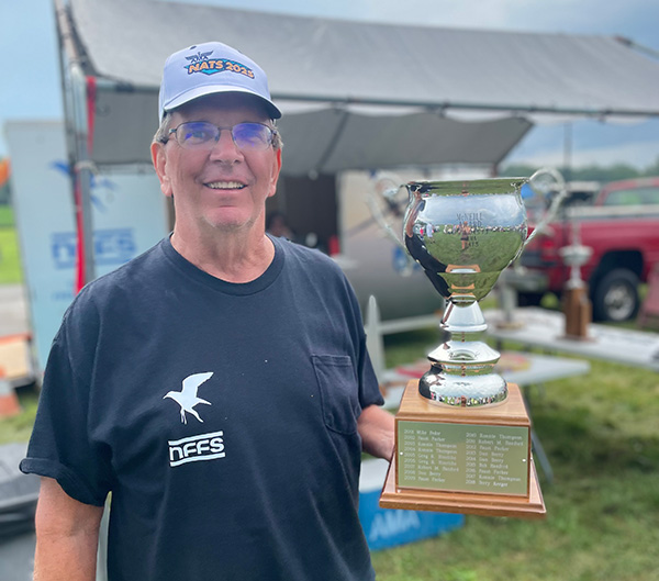 Man smiling, holding a large trophy outdoors.