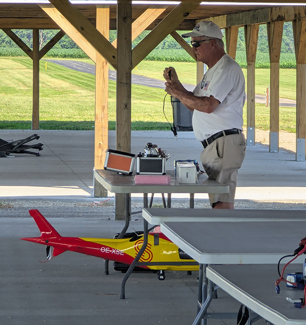 Man setting up equipment near model aircraft at outdoor pavilion.