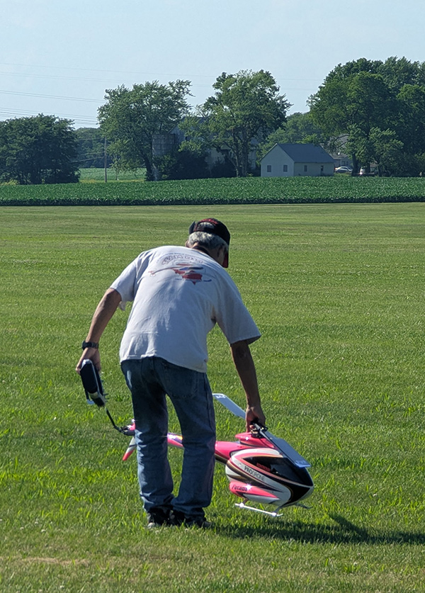 Man in a field holding a large RC helicopter and a controller.