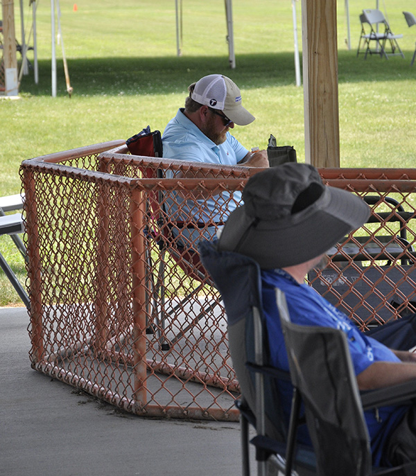 Two men seated in a shaded area at a park, one wearing a large sun hat.