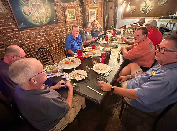 Group dining at a long table in a warmly lit restaurant.