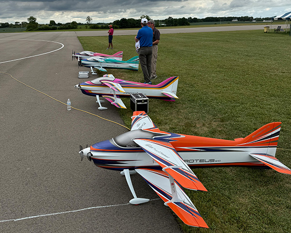 Model airplanes lined up on a runway, two people standing nearby.