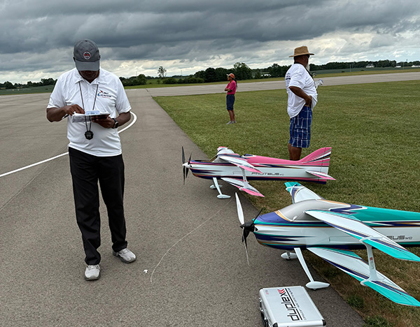 Remote-controlled airplanes on a runway, with people standing nearby.