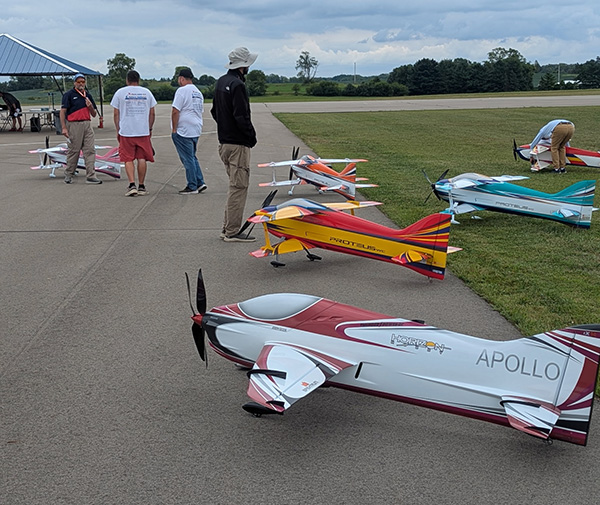 Model airplanes on ground, people nearby chatting on airfield.