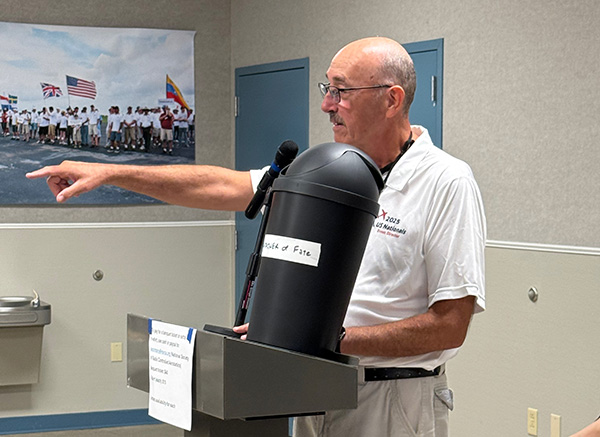 Man pointing while speaking at a podium, wearing a white shirt.