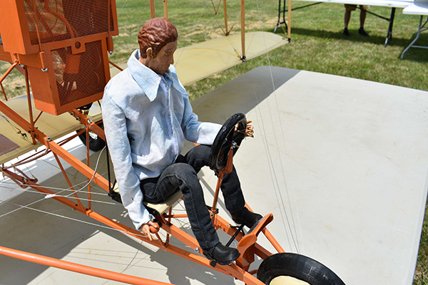 Model of early aviator sitting in replica plane on grass.