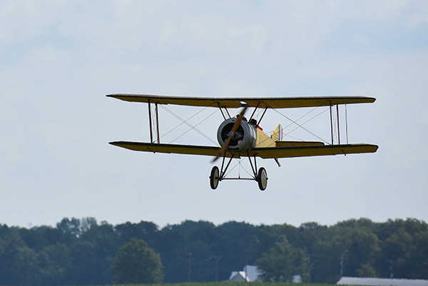 Vintage biplane flying over rural landscape.