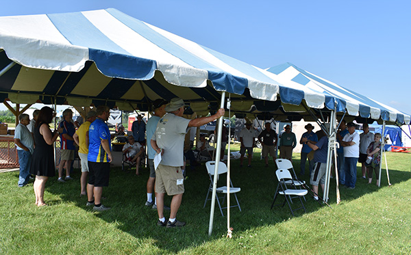 Outdoor gathering under blue and white striped tent on grass.