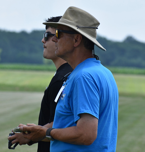 Two people wearing sunglasses control a drone outdoors.
