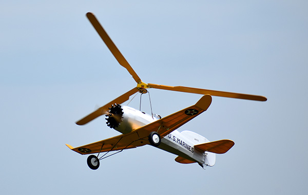 Vintage biplane with yellow wings flying in a clear blue sky.