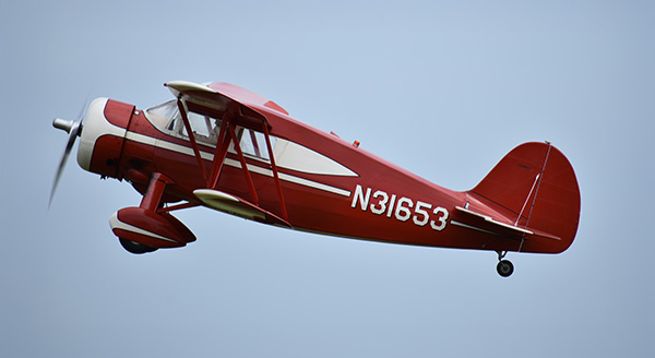 Red vintage airplane flying against a clear blue sky.