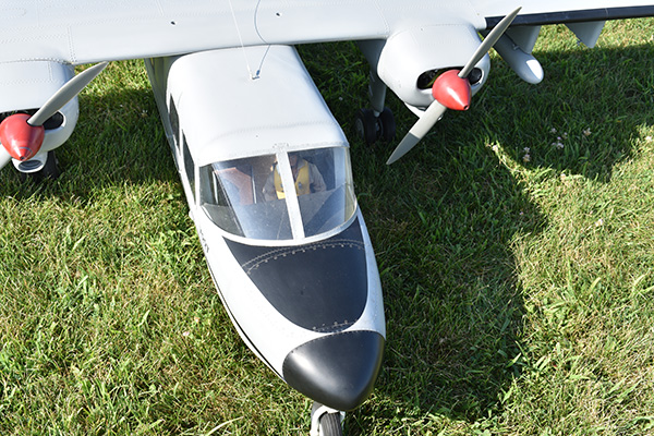 Model airplane on grass with white fuselage and red-tipped propellers.